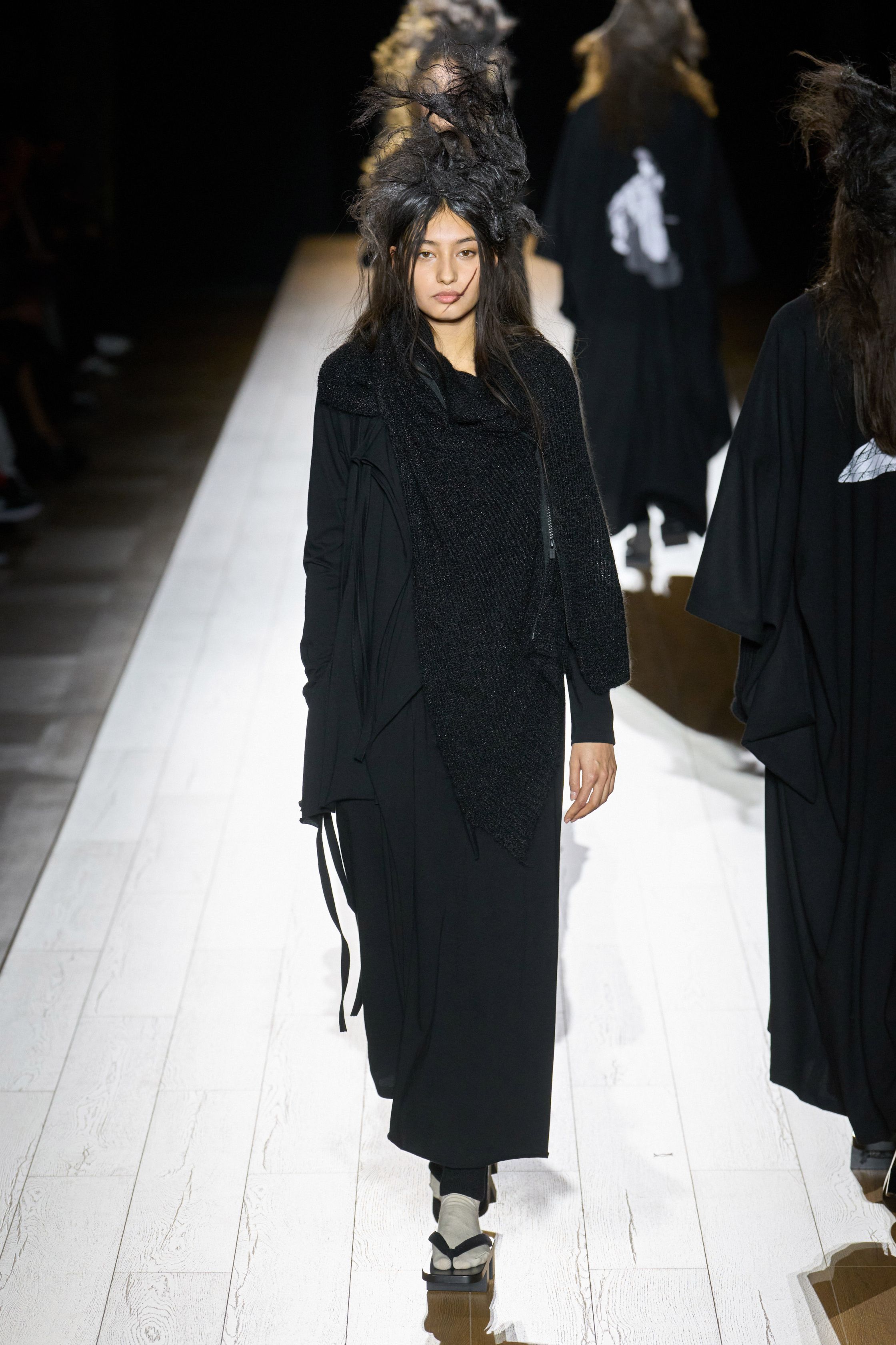 Yohji Yamamoto 本季依然延续标志性的黑色哲学：宽松层叠轮廓、和服式结构与手工拼接面料形成一种诗意而深沉的东方美学。夸张头饰与飘逸衣摆让整场秀像一场黑色戏剧，既神秘又极具艺术感-顽石频道趋势研究